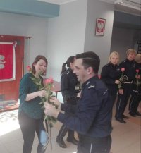 Na zdjęciu mężczyzna w policyjnym mundurze wręcza kwiaty kobiecie.