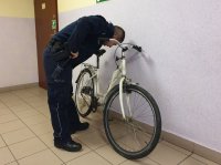 Na zdjęciu policjant w mundurze kontroluje rower w kolorze białym na korytarzu lublinieckiej komendy .