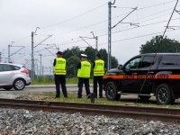 Na zdjęciu umundurowany policjant w czasie akcji &quot;Bezpieczny przejazd&quot; stojący wraz z dwoma umundurowanymi Strażnikami Ochrony Kolei na terenie przejazdu kolejowego..