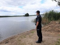 Na zdjęciu policjant w mundurze stojący nad brzegiem jeziora.